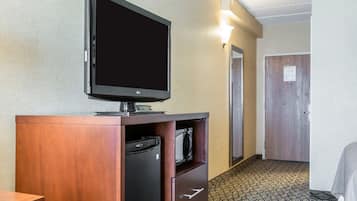 Une chambre d’hôtel équipée d’un téléviseur à écran plat posé sur un meuble en bois, d’un mini-réfrigérateur et d’un four à micro-ondes. On y trouve une porte avec une lumière au-dessus et un tapis à motifs.