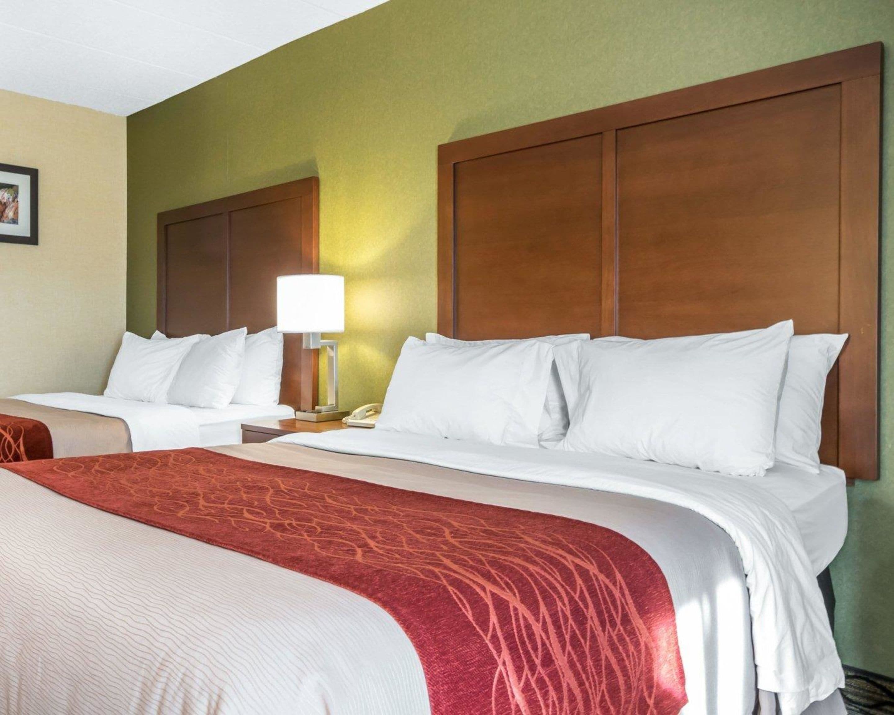 A hotel room with two beds, a wooden headboard, a nightstand with a lamp, and a telephone.