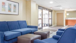 A waiting area with blue sofas and a brown ottoman, a reception desk, and a door leading to a hallway. - Comfort Inn Winchester (Winchester)