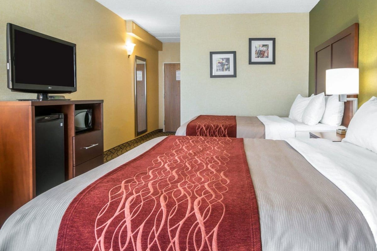 A hotel room with two beds, a television, a desk, and a lamp.