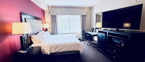 A hotel room with a bed, desk, television, and a window with curtains.