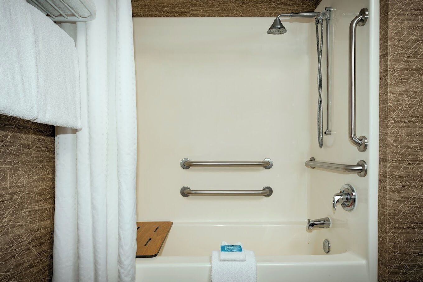 A bathroom with a bathtub, grab bars, a showerhead, and a towel rack.