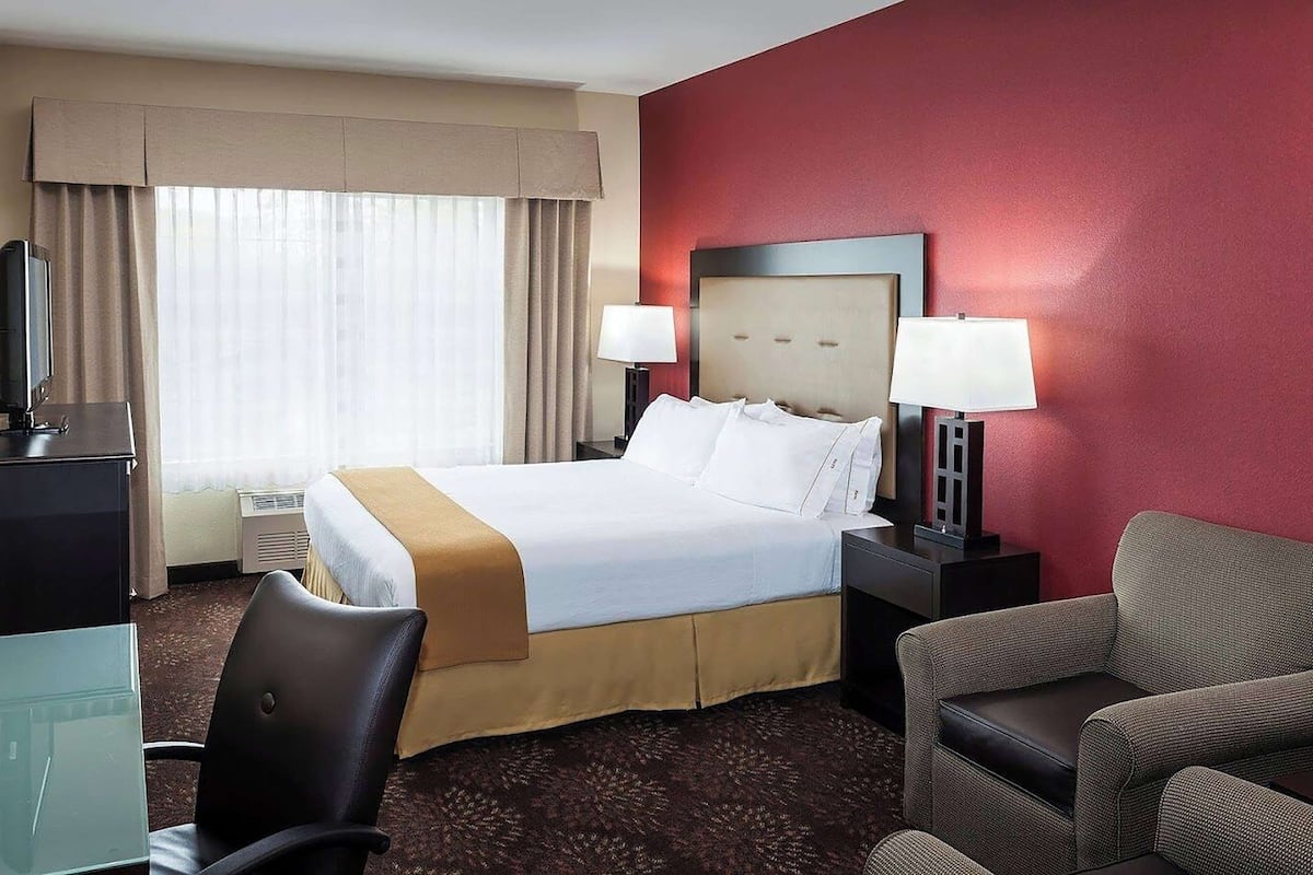 Une chambre d’hôtel avec un lit, deux lampes de chevet, un bureau avec un ordinateur, une chaise et un mur d’accent rouge.