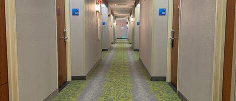 A hotel hallway with doors numbered 321 and 320, carpeted in green and gray, and wooden doors with a beige frame.