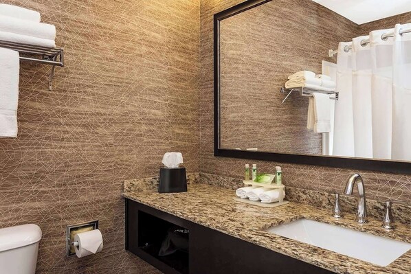 A bathroom with a marble countertop, a sink, a mirror, and towels on a rack.