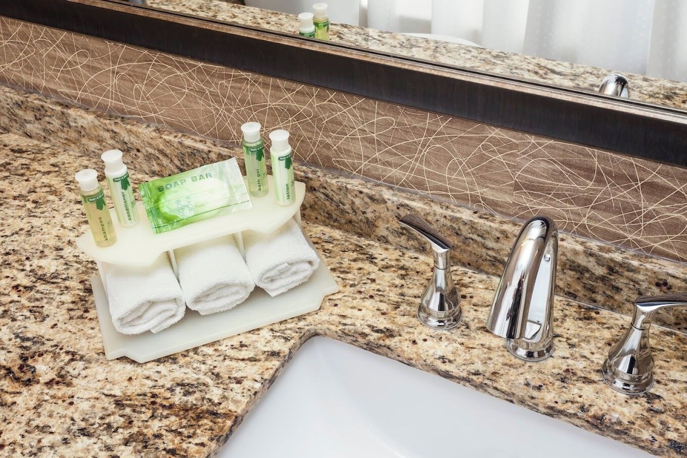 Bagno con piano di lavoro in granito, lavandino, specchio e porta sapone con flaconi.