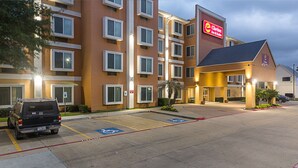 Ett hotell med en parkeringsplats, parkeringsplatser anpassade för personer med funktionsnedsättning och en byggnad med många fönster och en skylt för Clarion Inn & Suites.