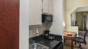 Ett kompakt hotellkök med mikrovågsugn, kaffebryggare och ett litet matbord med en stol.