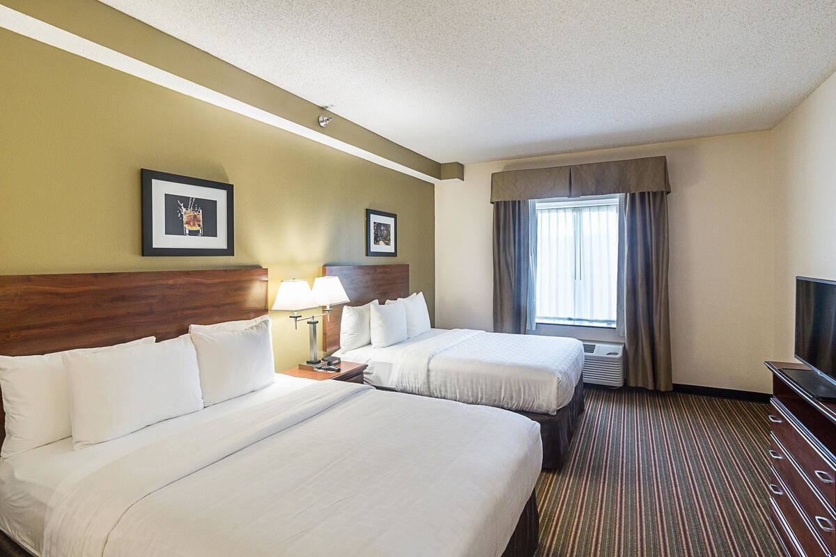 A hotel room with two beds, a TV, and a window with curtains.
