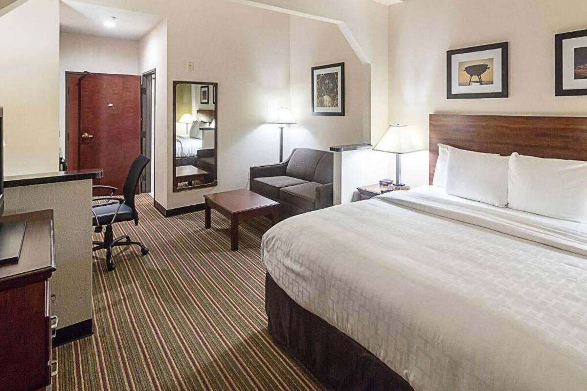 A hotel room with a bed, desk, chair, and a lamp.