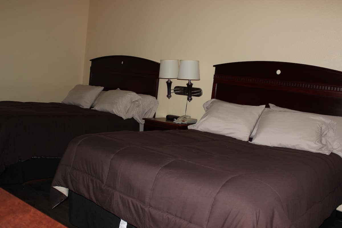 A hotel room with two beds, each with a wooden headboard, a nightstand with a lamp, and a telephone.