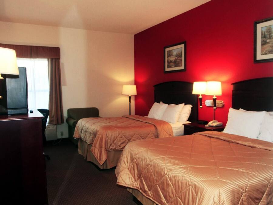 A hotel room with two beds, a desk, and a chair. There are two bedside lamps and a telephone on the nightstand.