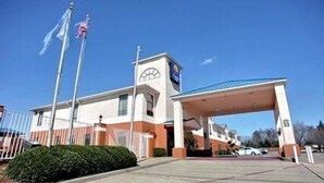 A hotel with a covered entrance, a flagpole with flags, and a clear blue sky. - Truckerz Inn (Jacksonville)