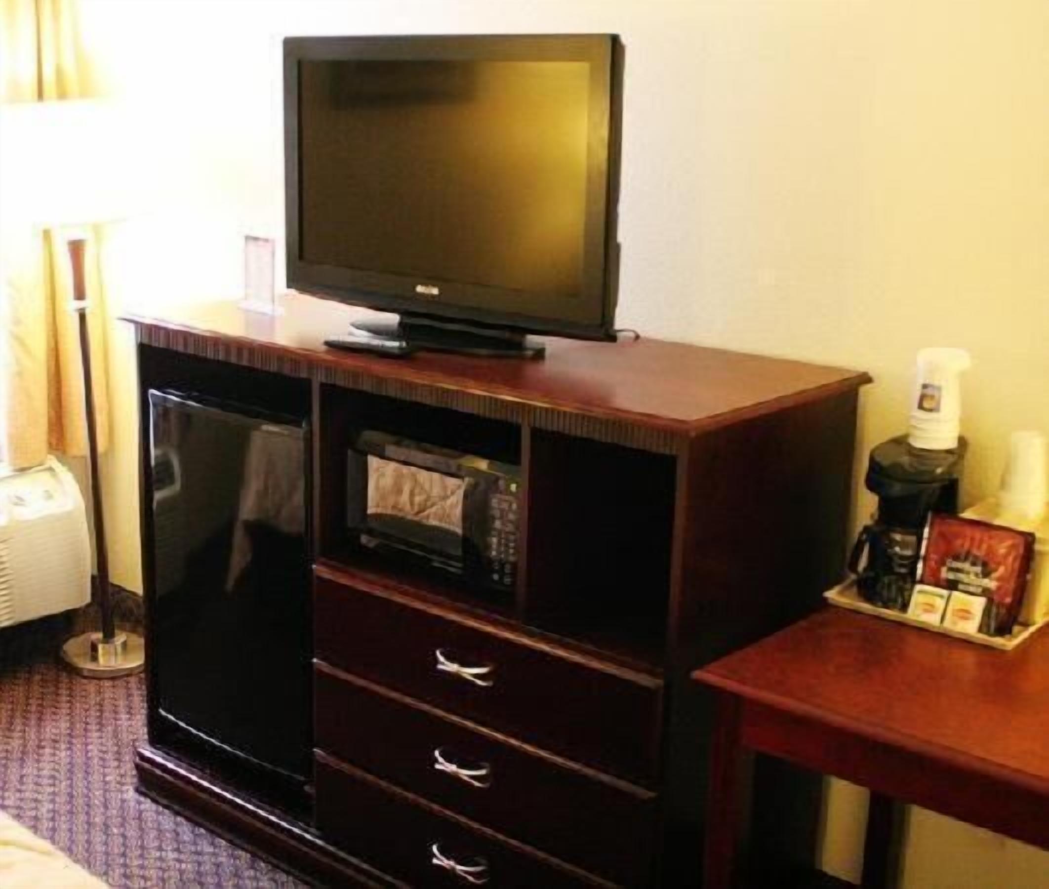 Habitación de hotel con televisor en un mueble de madera, microondas y una mesita con artículos de aseo.
