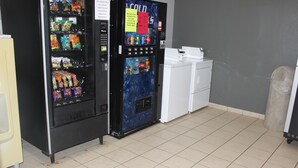 A vending machine with snacks and drinks, a small refrigerator, and a trash can in a room with tiled flooring. - Truckerz Inn (Jacksonville)