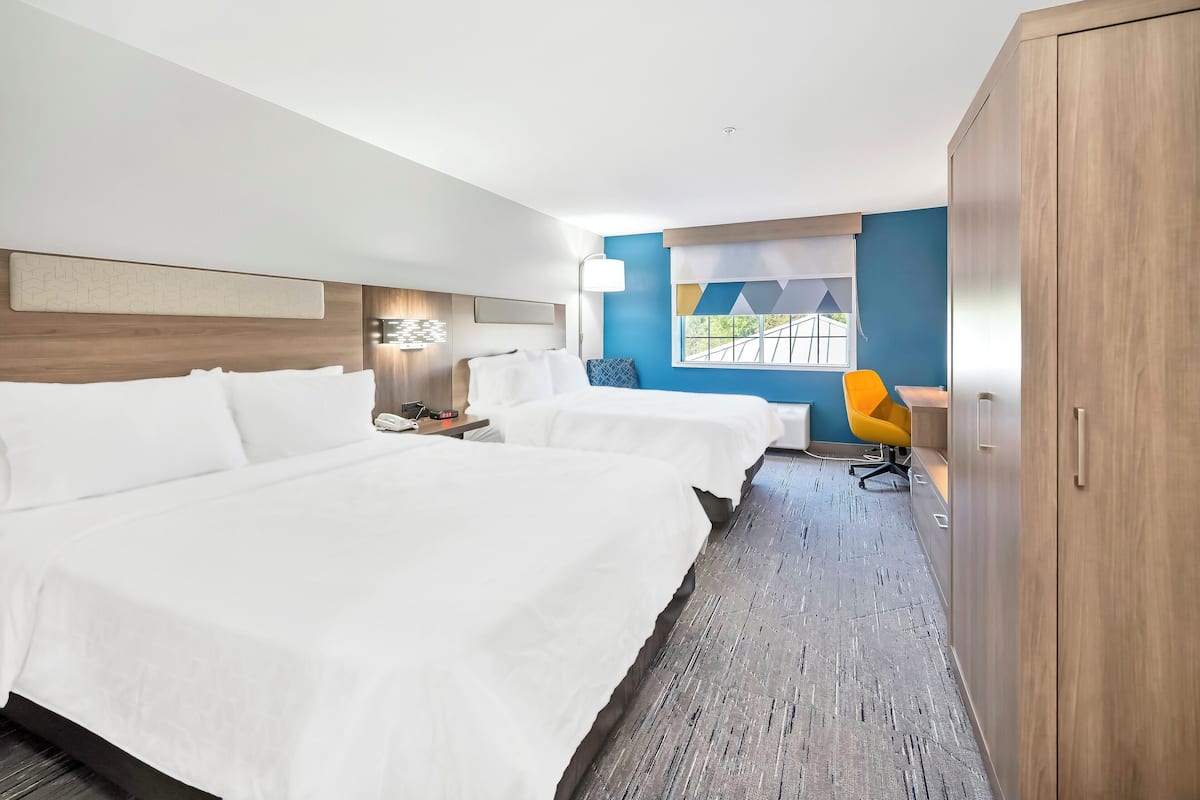 Habitación de hotel con dos camas, un armario de madera, un escritorio con silla y una ventana con vistas.