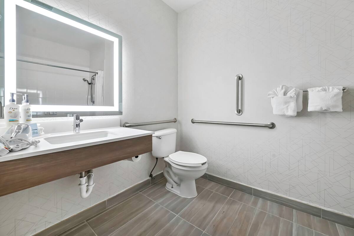 Un baño moderno con un espejo grande, un lavabo, un inodoro y una ducha.