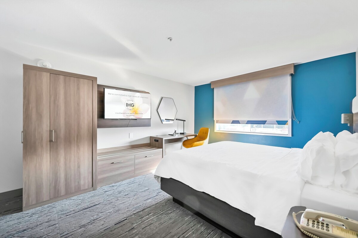Une chambre d’hôtel moderne équipée d’un lit, d’un bureau, d’une chaise, d’une télévision et d’une armoire.