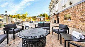 Un espace patio avec des sièges d’extérieur, une table ronde et une piscine en arrière-plan.