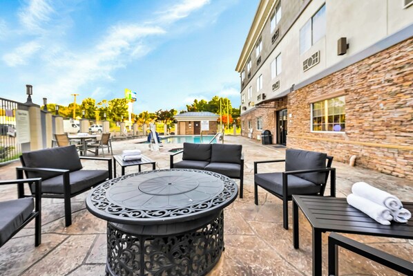 Un espace patio avec des sièges d’extérieur, une table ronde et une piscine en arrière-plan.