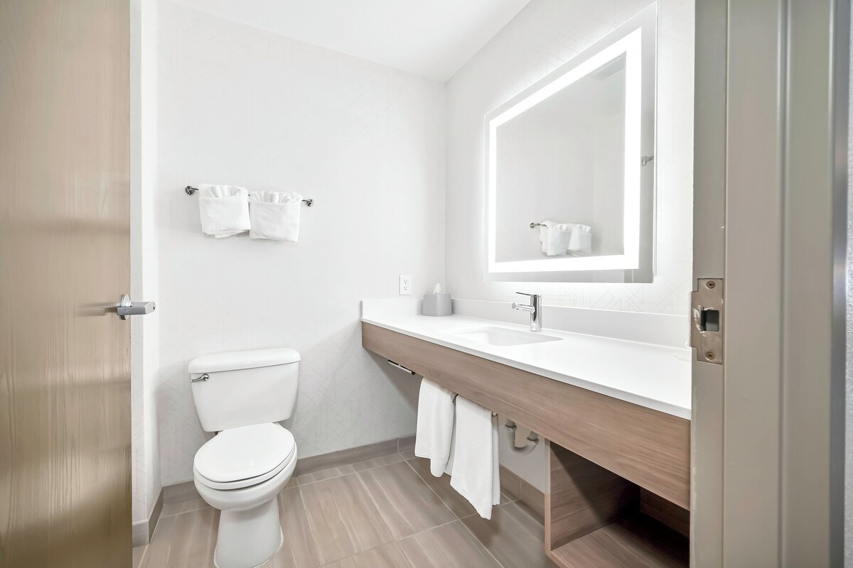 Une salle de bain moderne avec des toilettes blanches, un grand miroir et un meuble-lavabo en bois avec un évier.