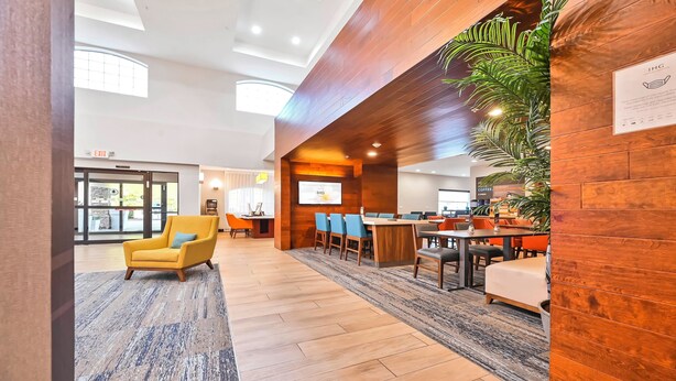 A modern hotel lobby with wooden paneling, a seating area with tables and chairs, and a large screen displaying information. - Holiday Inn Express Palestine by IHG (Palestine)