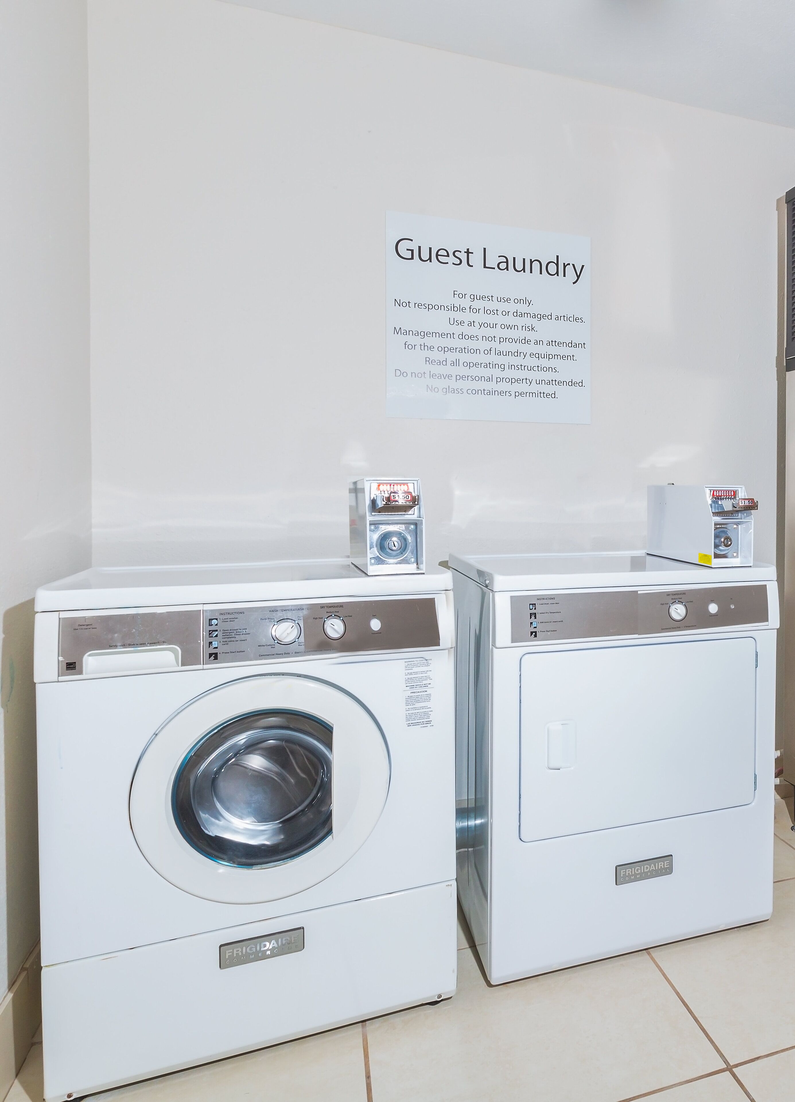 Deux machines à laver à chargement frontal sont installées dans une buanderie, avec une pancarte placée au-dessus.