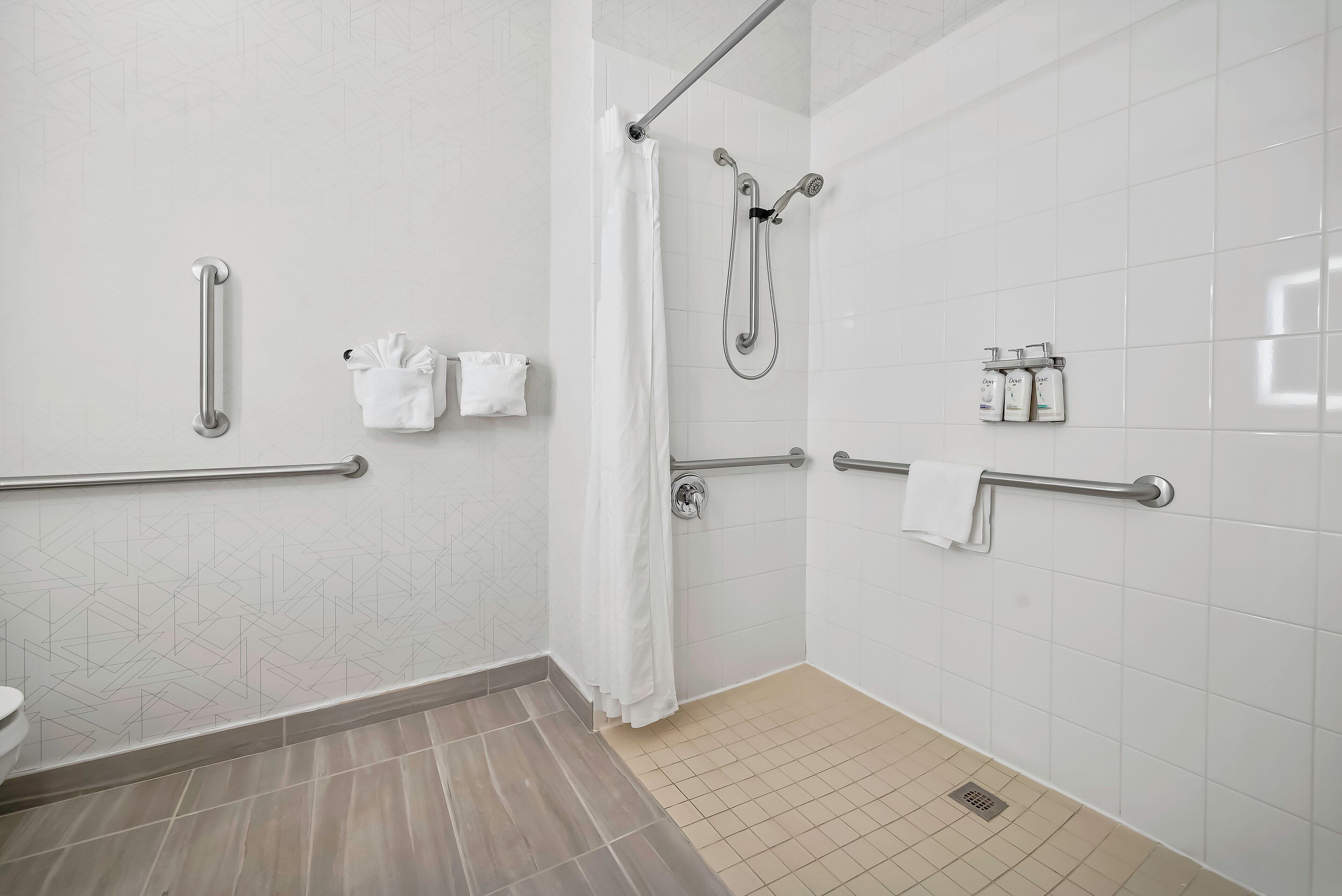 Un baño moderno con ducha, barras de apoyo y un inodoro.