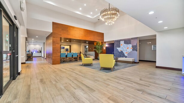 Un hall d’entrée spacieux avec un plancher en bois, des chaises jaunes, un lustre moderne et une fresque représentant une carte géographique sur le mur.