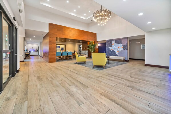 Un hall d’entrée spacieux avec un plancher en bois, des chaises jaunes, un lustre moderne et une fresque représentant une carte géographique sur le mur.