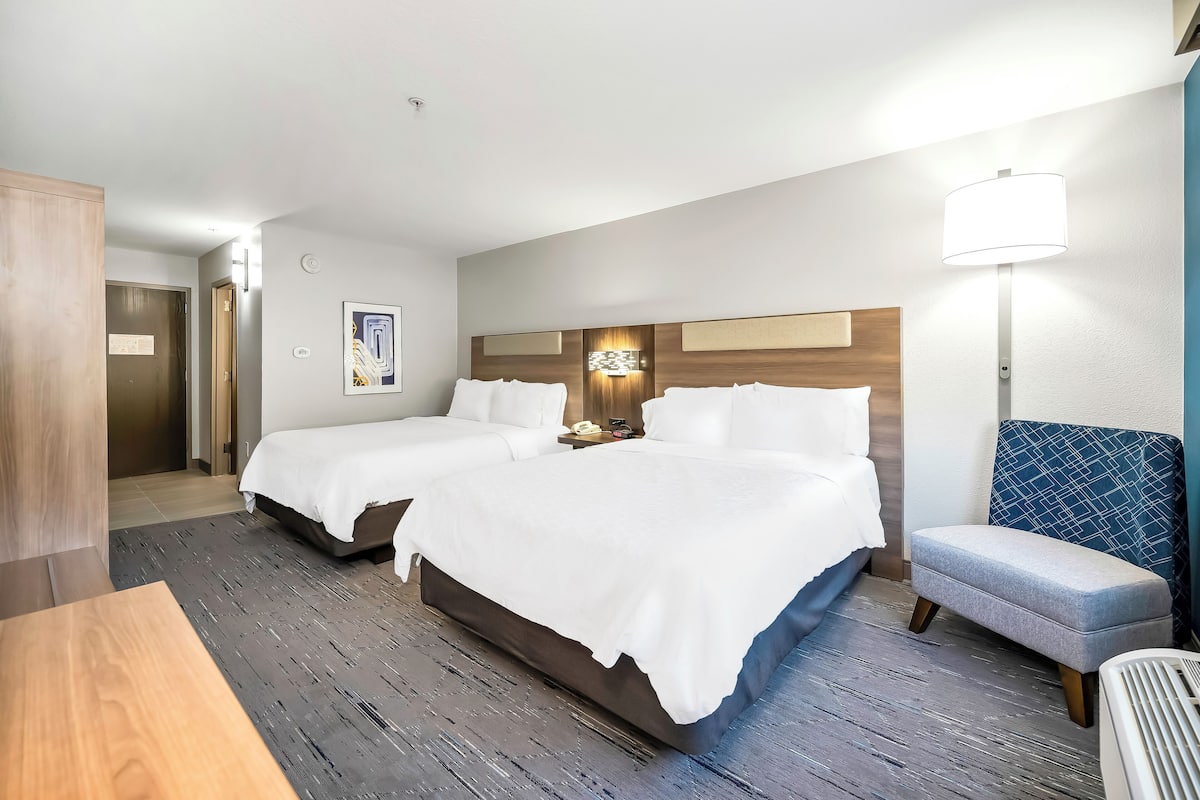 Una habitación de hotel con dos camas, un escritorio, una silla y una lámpara.