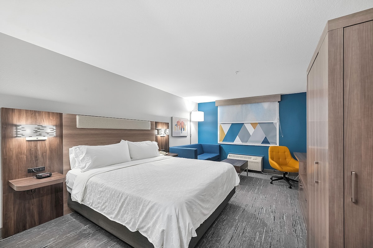 Una habitación de hotel moderna con una cama grande, un escritorio, una silla y un armario.