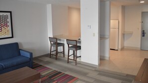 A living room with a blue sofa, a coffee table, and a colorful striped rug. There is a small dining area with a table and three chairs. A refrigerator is visible in the background. - Holiday Inn Express & Suites Batesville by IHG (Batesville)