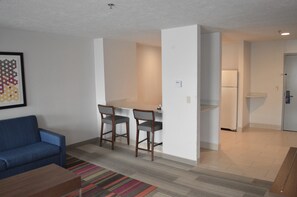 A living room with a blue sofa, a coffee table, and a colorful striped rug. There is a small dining area with a table and three chairs. A refrigerator is visible in the background. - Holiday Inn Express & Suites Batesville by IHG (Batesville)