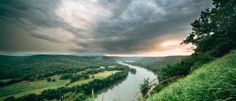 A river winding through a lush valley with dense greenery and a dramatic sky.