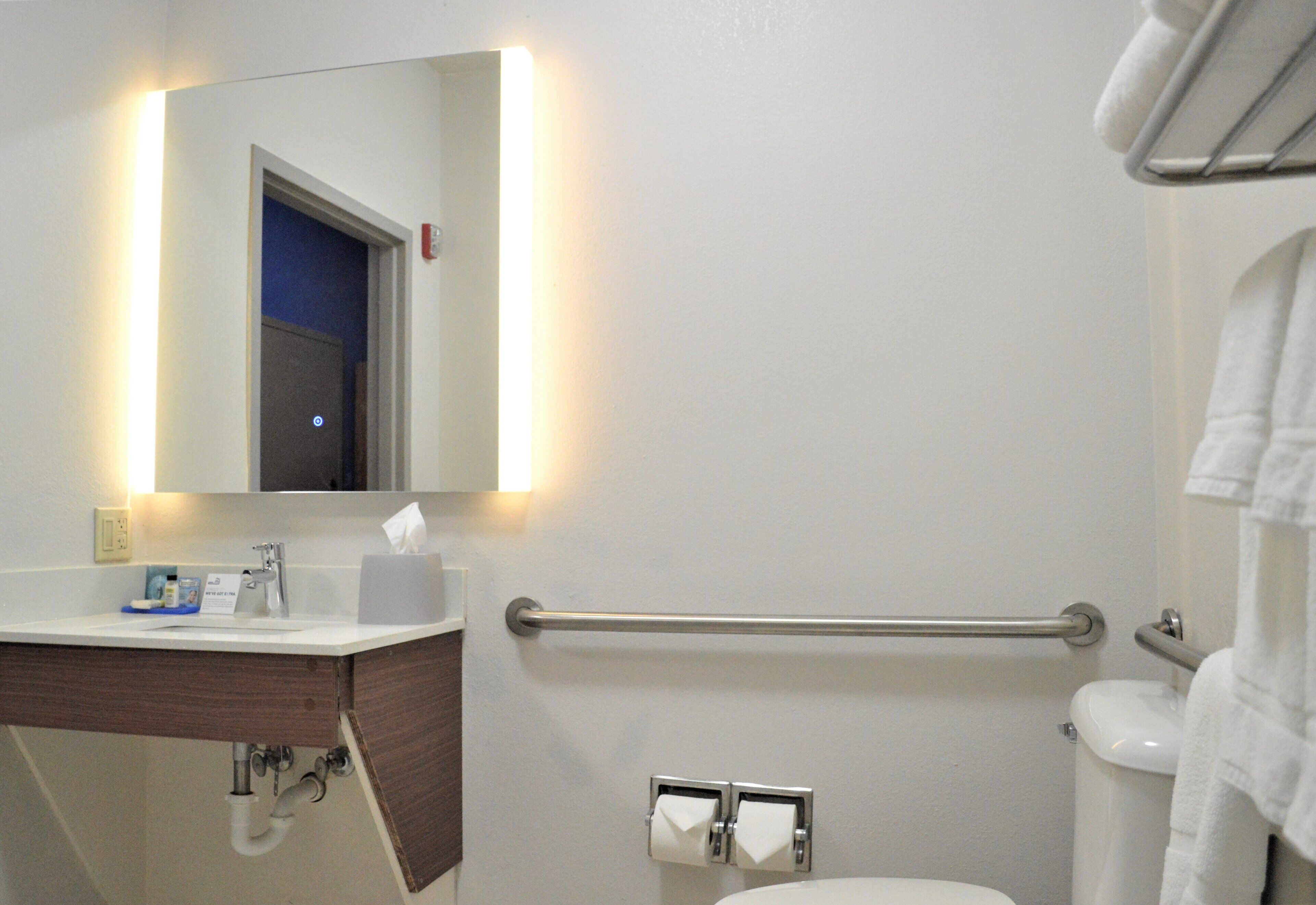 A bathroom with a white sink, mirror, and toilet. There is a towel rack on the wall and a handrail for accessibility.