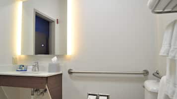 A bathroom with a white sink, mirror, and toilet. There is a towel rack on the wall and a handrail for accessibility.