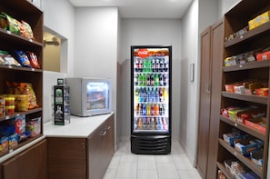 A vending machine with various beverages and snacks, located in a narrow hallway with shelves on either side. - Holiday Inn Express & Suites Batesville by IHG (Batesville)