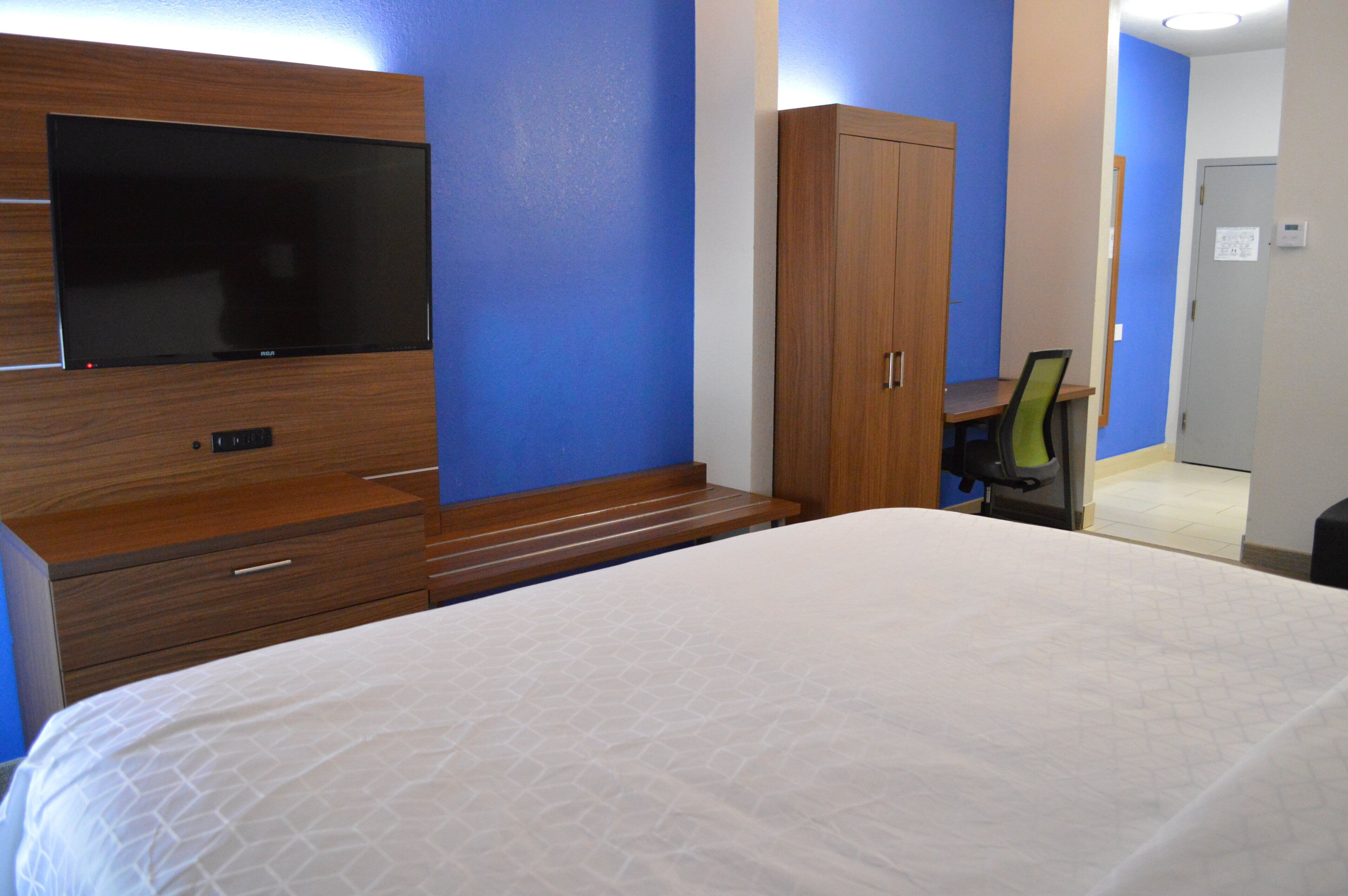 A hotel room with a bed, a TV, a wooden wardrobe, and a desk with a chair.