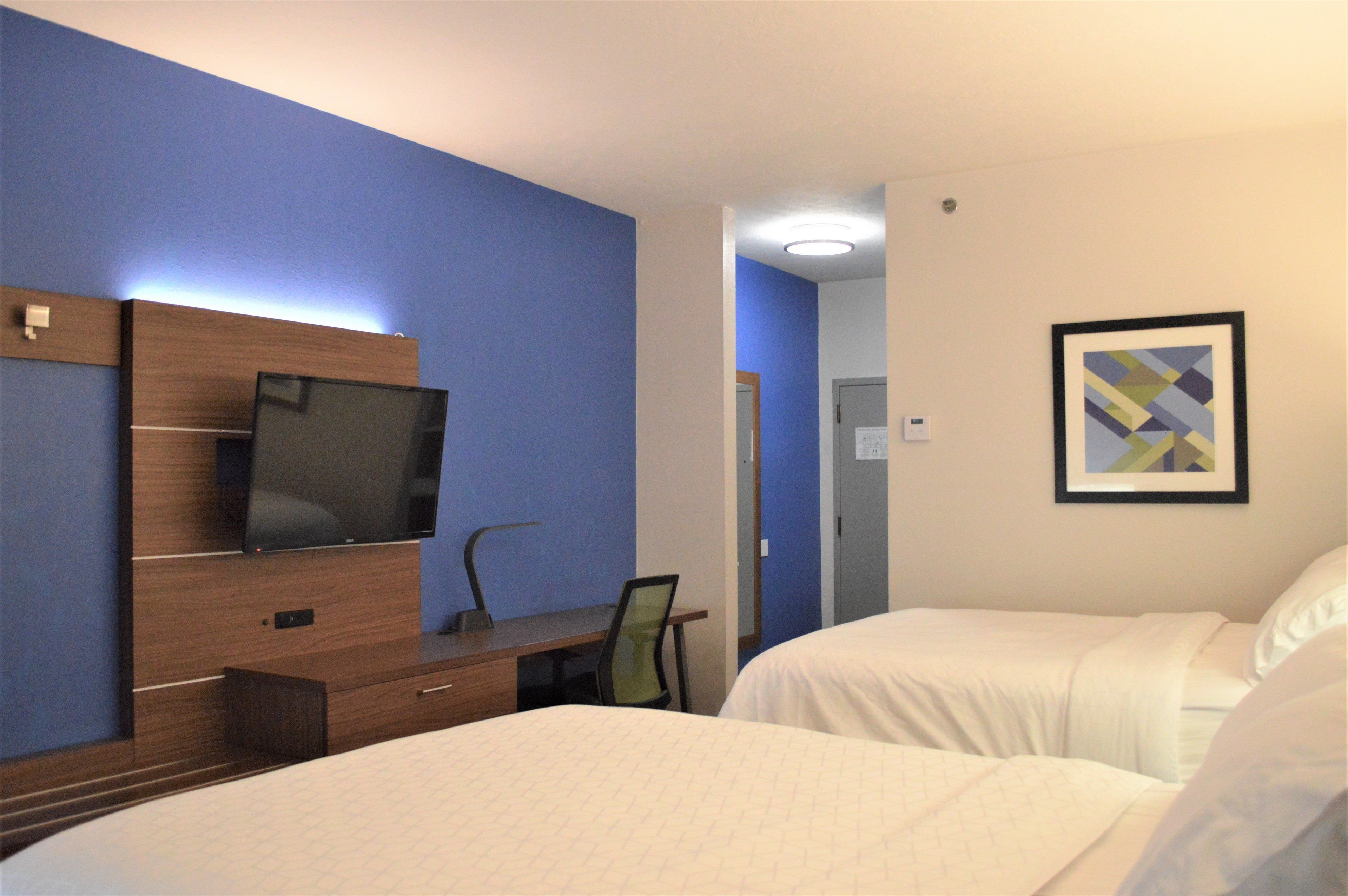 Habitación de hotel con una cama, un escritorio con una silla, un televisor y un cuadro en la pared.