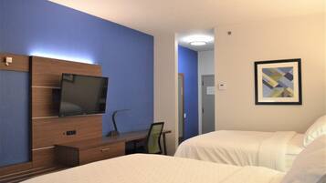 A hotel room with a bed, a desk with a chair, a television, and a framed picture on the wall.