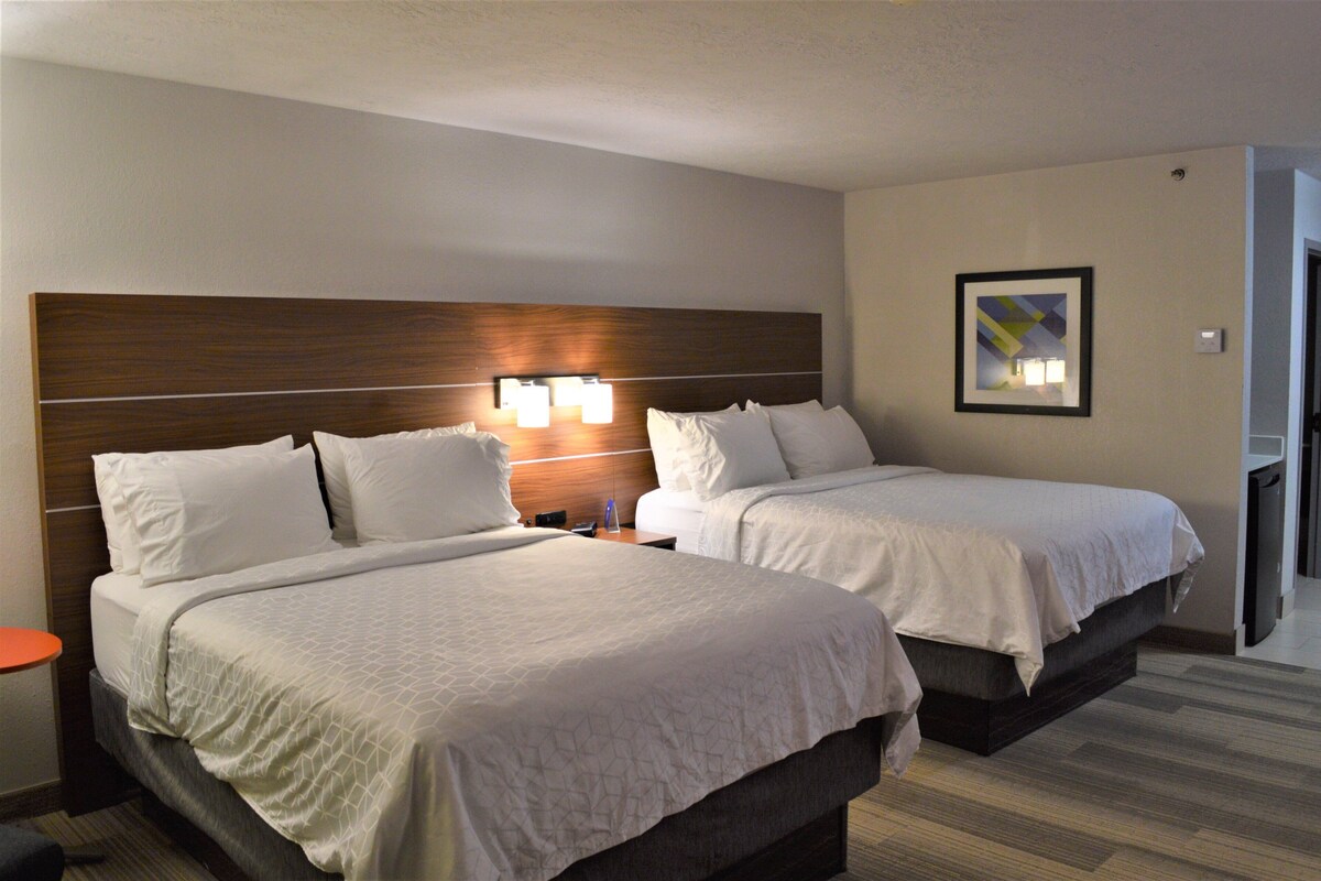 A hotel room with two beds, a nightstand, a small table, and a framed picture on the wall.