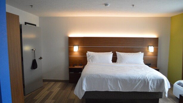 A hotel room with a large bed, a wooden headboard, bedside tables, and a wall-mounted heater. - Holiday Inn Express & Suites Batesville by IHG (Batesville)