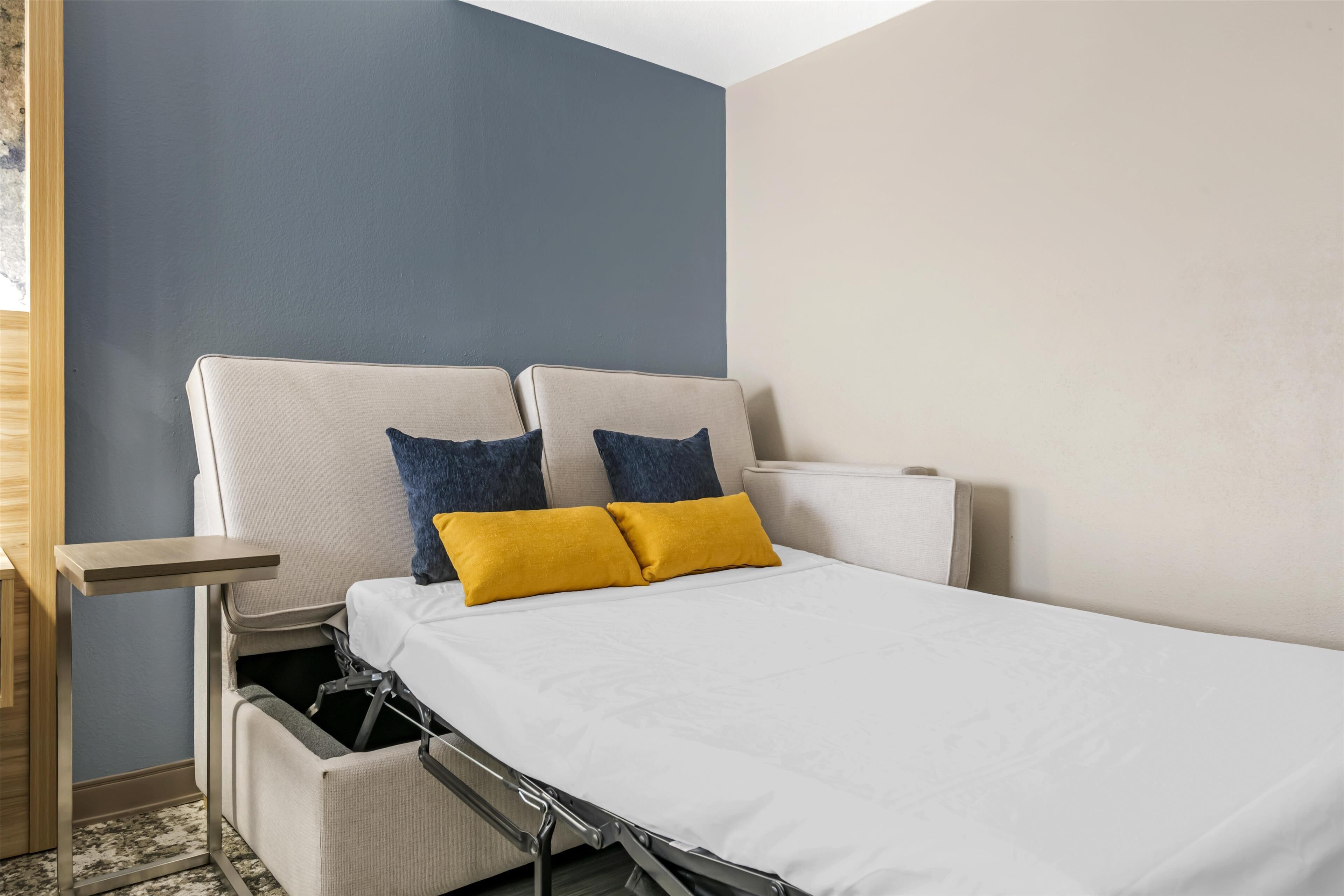 A compact bed with a headboard, two pillows, a bedside table, and a built-in storage unit.