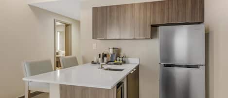 Una cocina moderna con refrigerador de acero inoxidable, armarios de madera y encimera blanca.