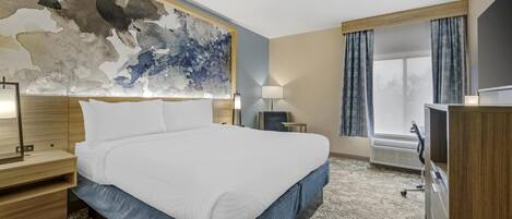 Una habitación de hotel con una cama grande, una mesita de noche, una lámpara, un televisor y una ventana con cortinas.