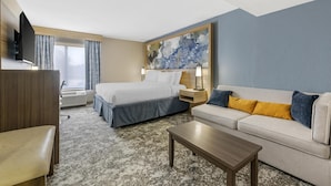 A hotel room with a bed, a sofa, a coffee table, a TV, and a painting on the wall.