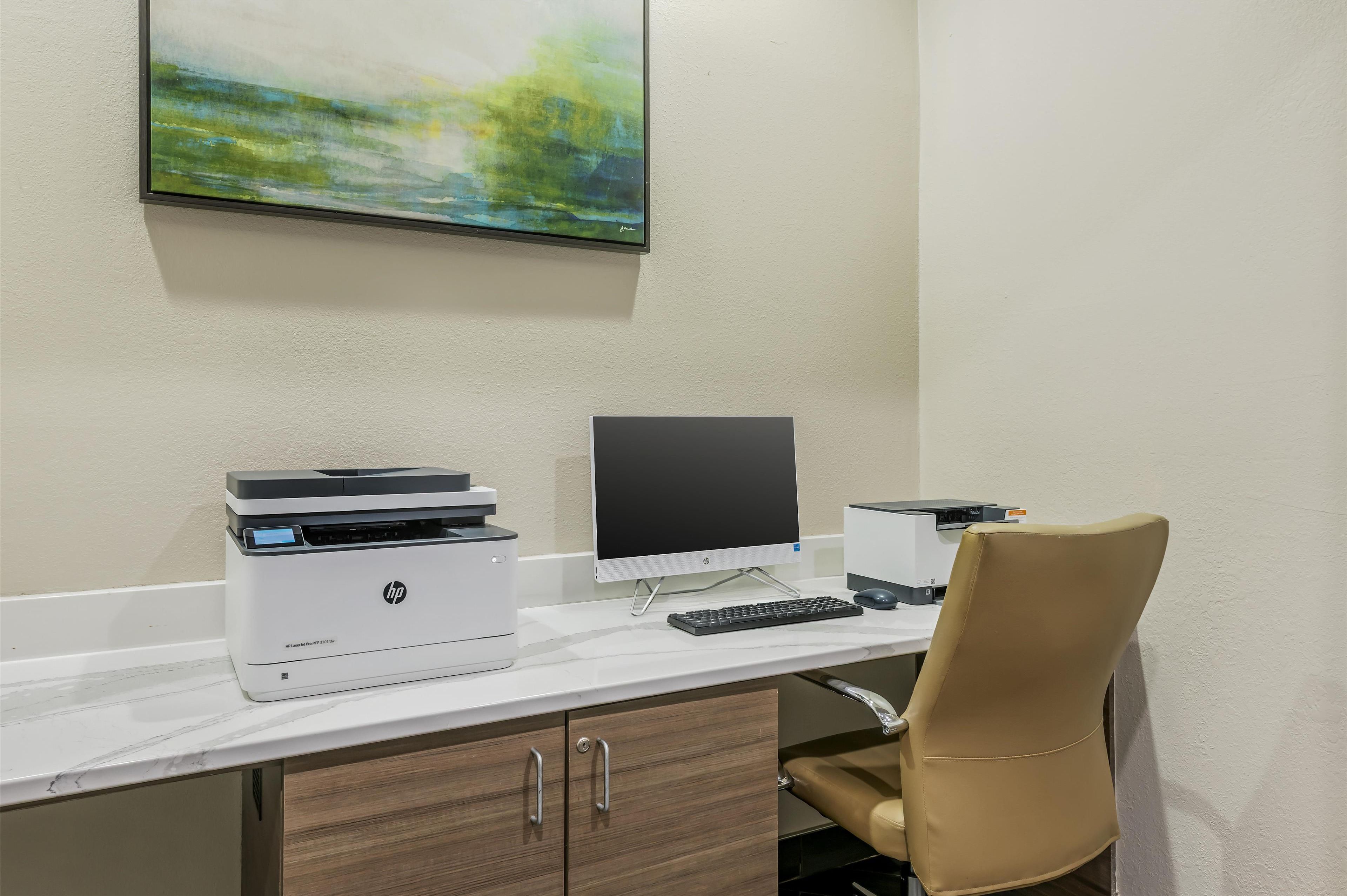 A modern office desk with an HP printer, a monitor, and a keyboard.