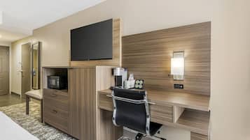 A hotel room with a wooden desk, a flat-screen TV, a microwave, a chair, and a bedside table.