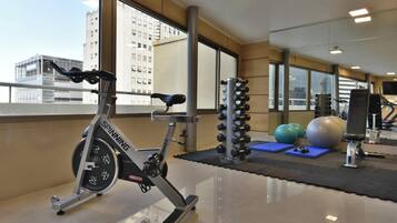 A gym with exercise equipment, including a spinning bike, dumbbells, and exercise balls.